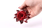 A hand holding a red sequin flower against a white background.