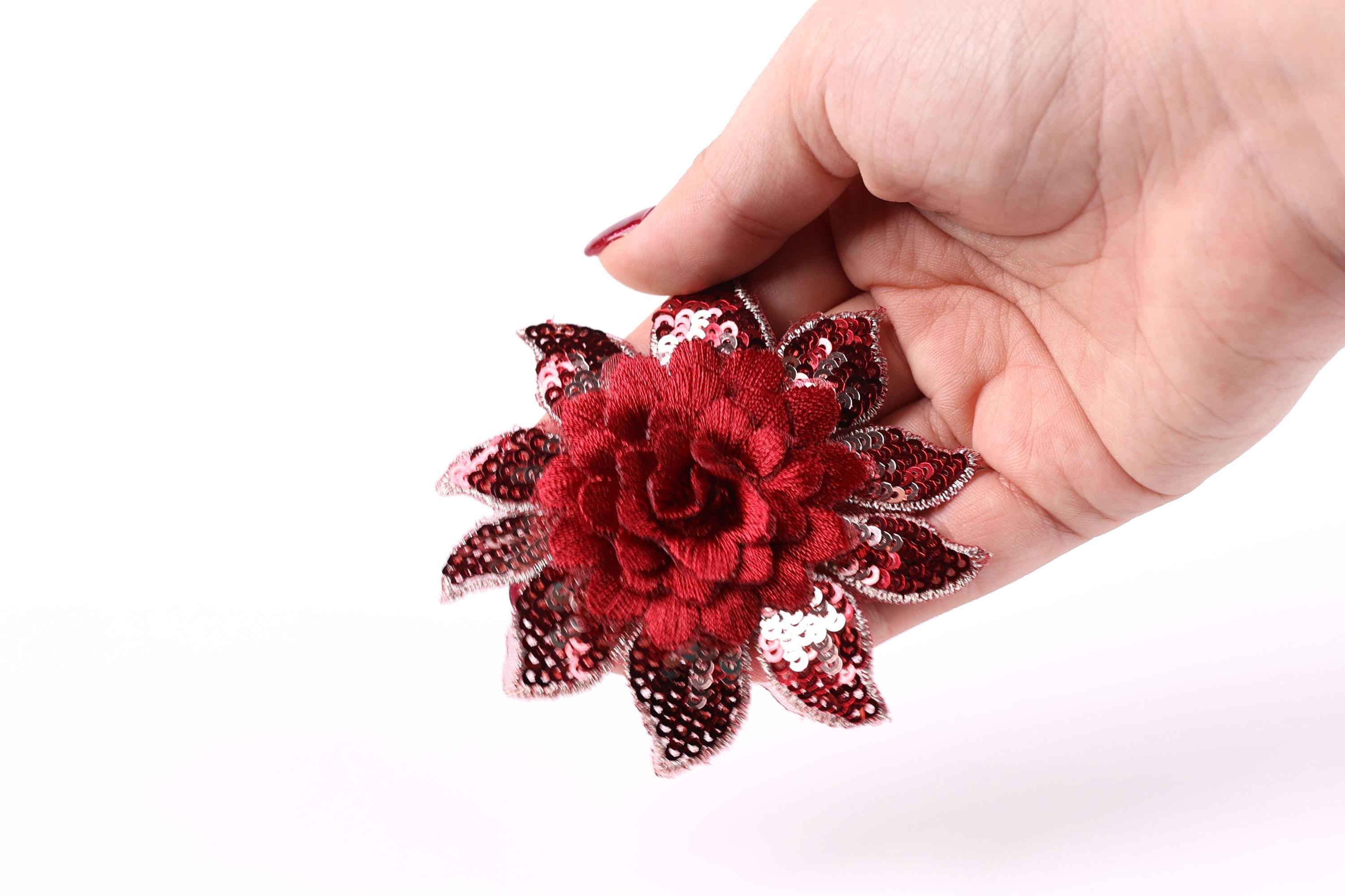 A hand holding a red sequin flower against a white background.