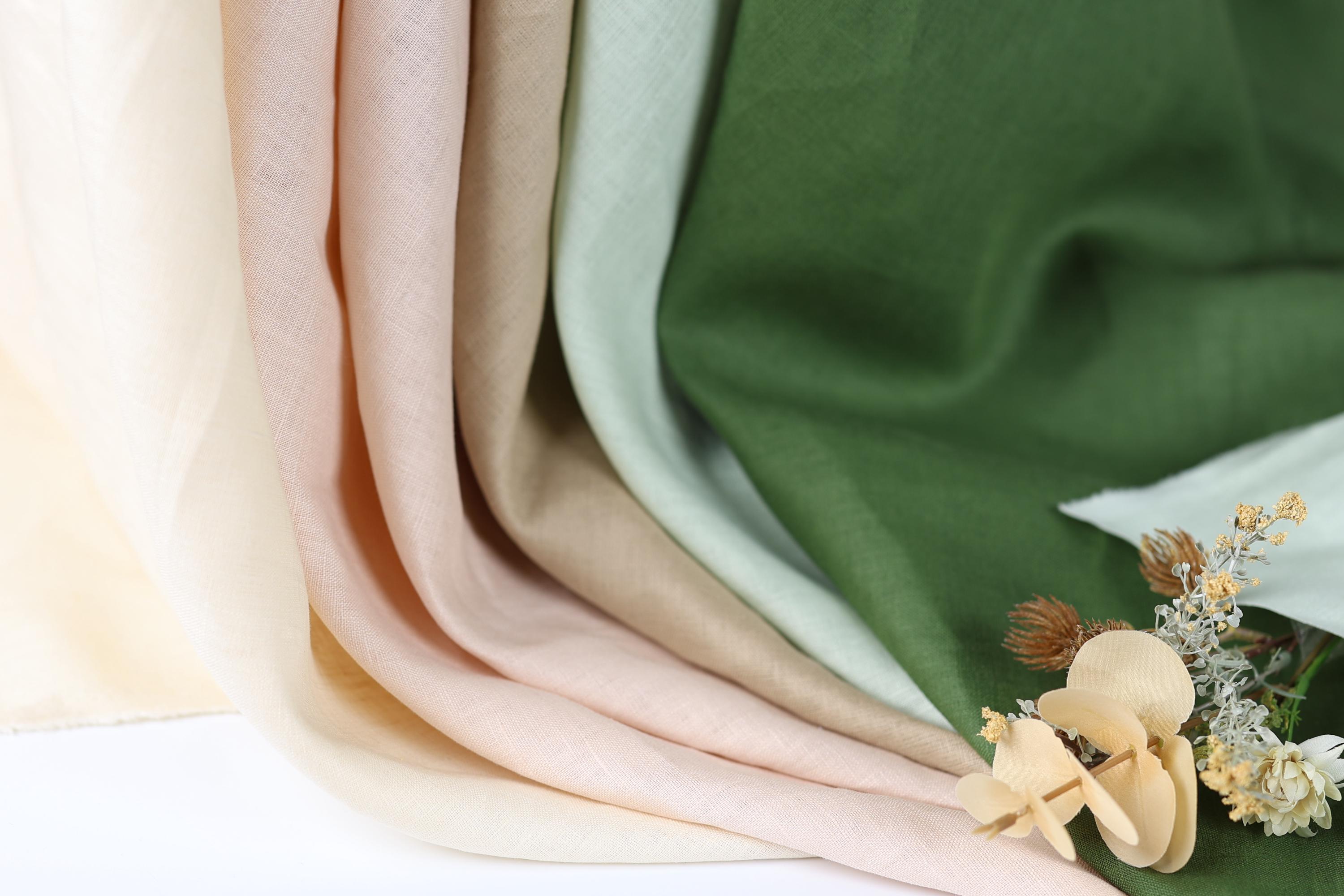 a close-up view of a fabric with a variety of colors, including green, beige, and peach. The fabric appears to be folded or rolled, creating a visually interesting composition. In addition to the fabric, there are small flowers or dried flowers visible in the image, adding a touch of natural beauty to the scene.