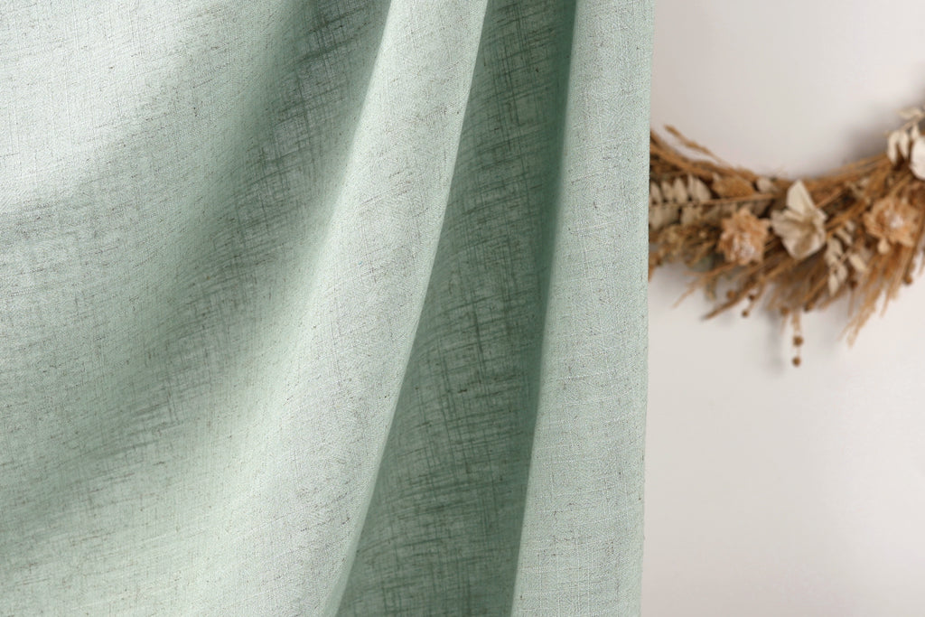 a close-up view of a light green fabric, possibly a curtain or textile, with a wreath made of dried flowers or branches on the right side of the frame.
