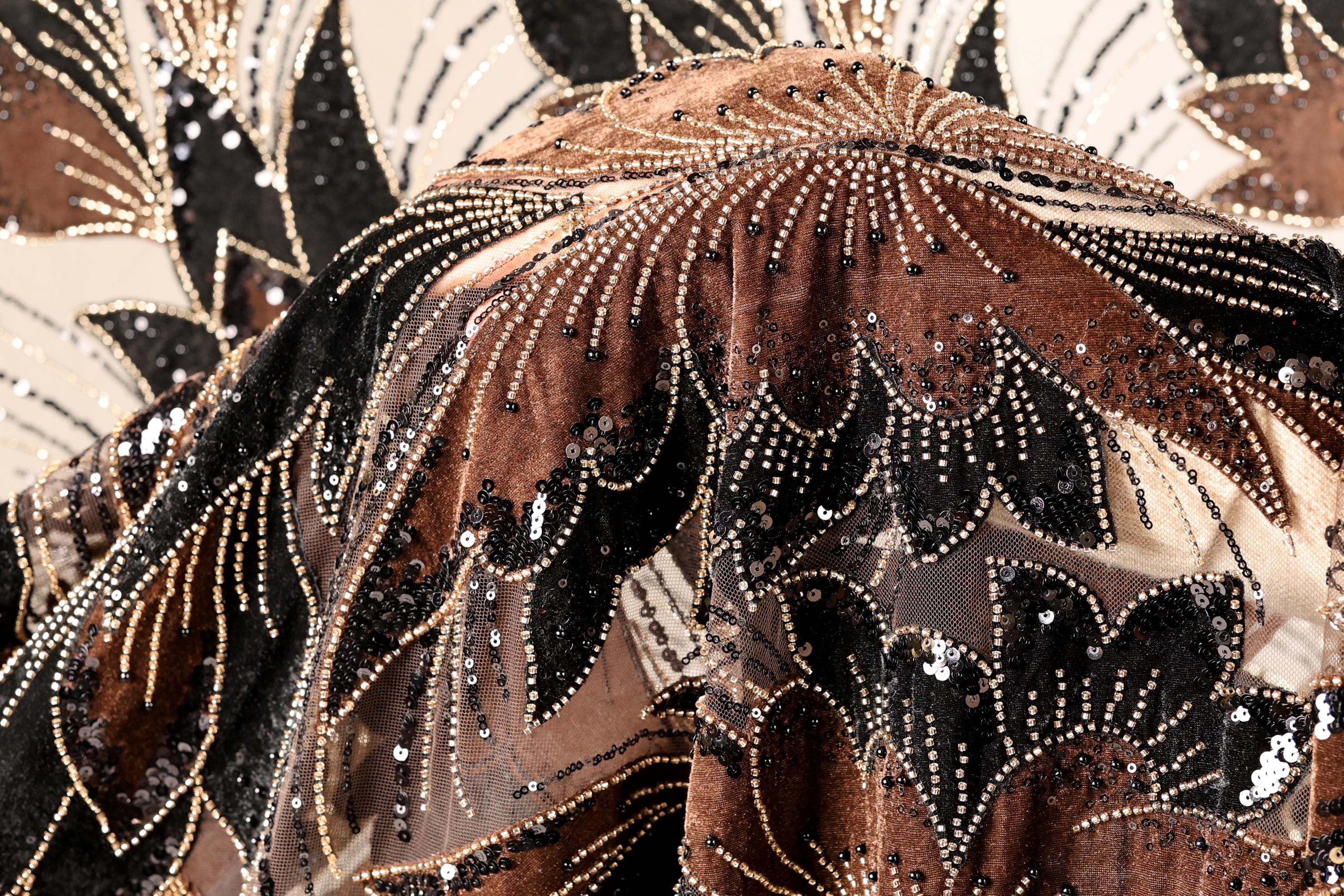 a close-up view of a fabric with a floral pattern, adorned with sequins and beads in shades of brown, black, and gold.