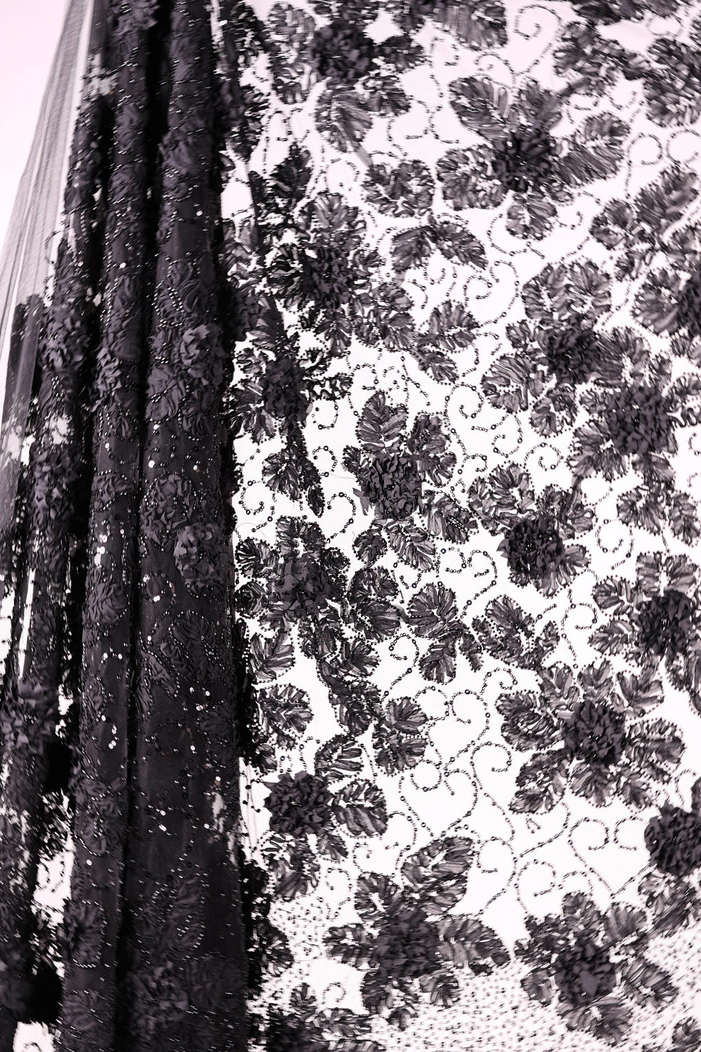 a close-up view of a black lace fabric with a floral pattern. The lace appears to be made of a shiny material, and the intricate design of the lace is visible, with the individual threads creating a visually striking pattern.