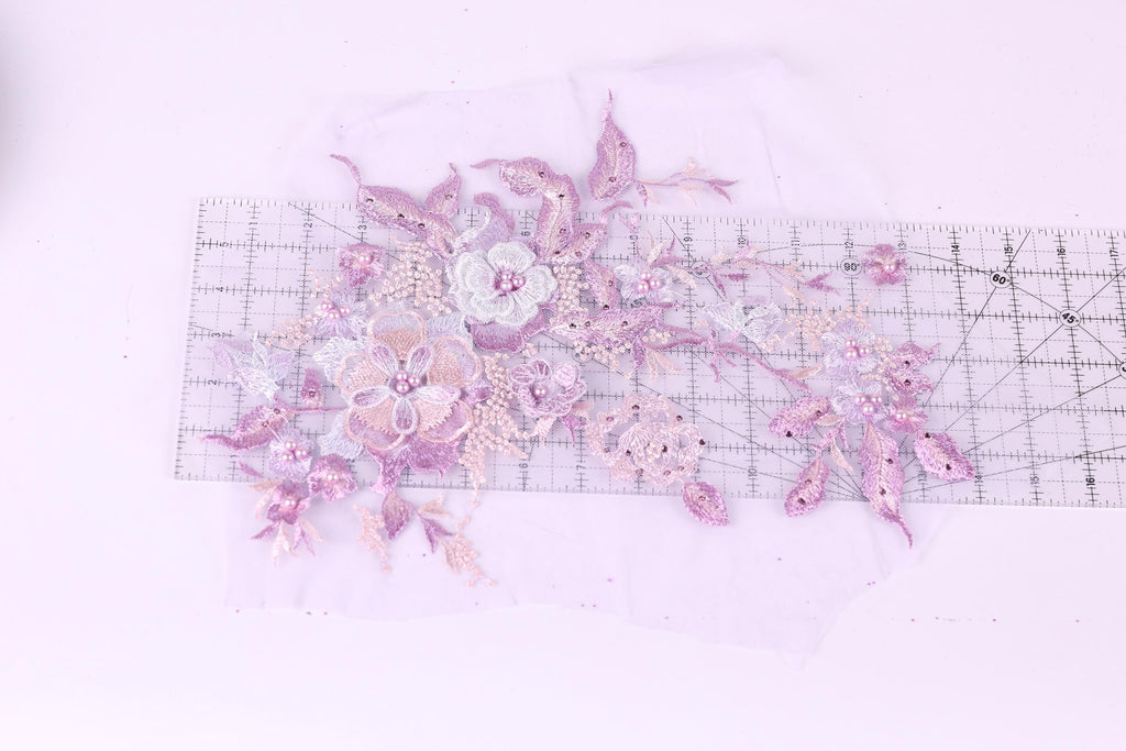 a close-up view of a delicate floral embroidery design, with various shades of pink and purple flowers and leaves. The design is displayed on a transparent surface, allowing for a clear view of the intricate details.