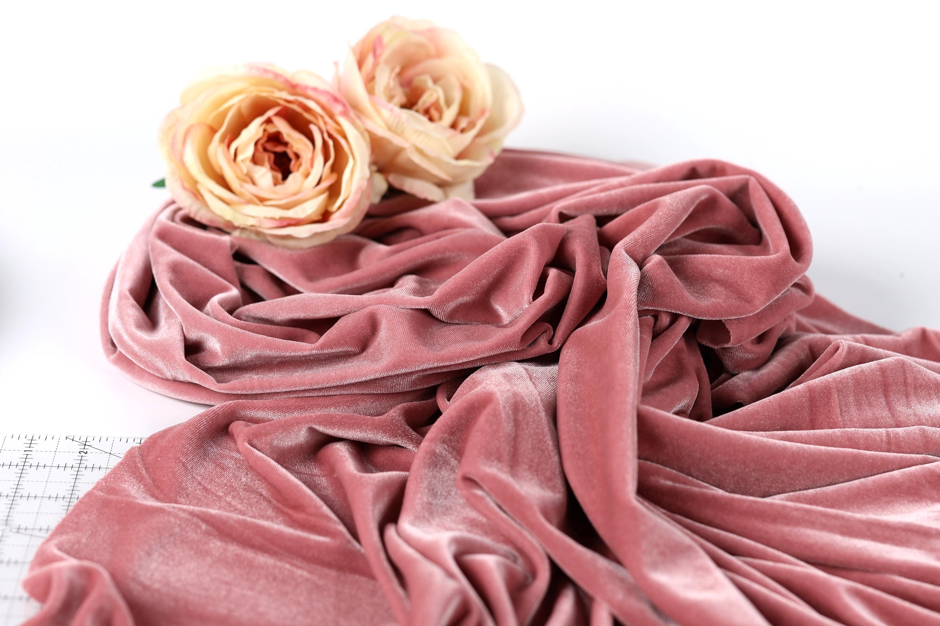 a close-up view of a pink velvet fabric with two peach-colored roses resting on top of it.
