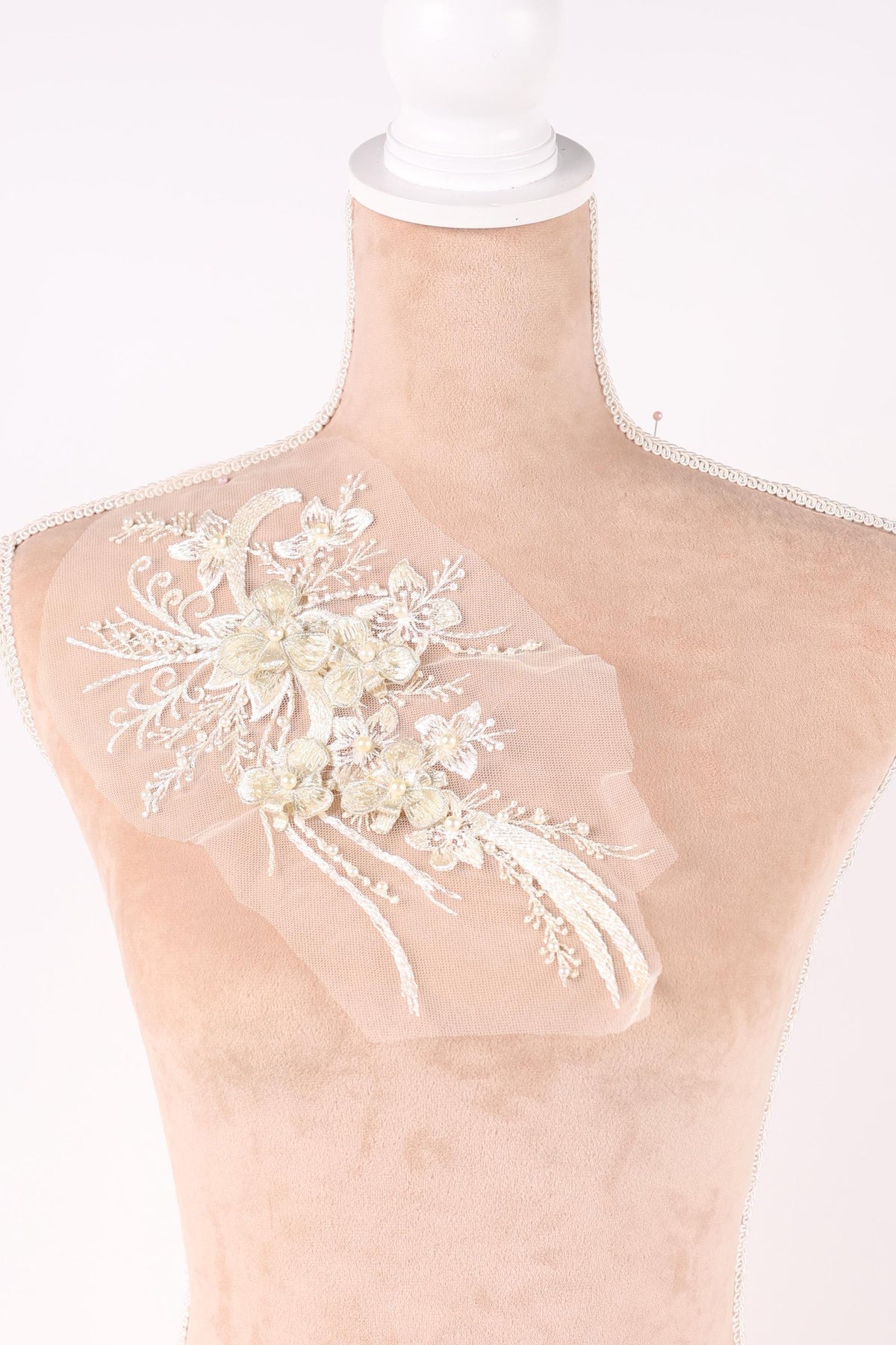 A close-up view of a delicate, white lace flower embroidered on a fabric surface.