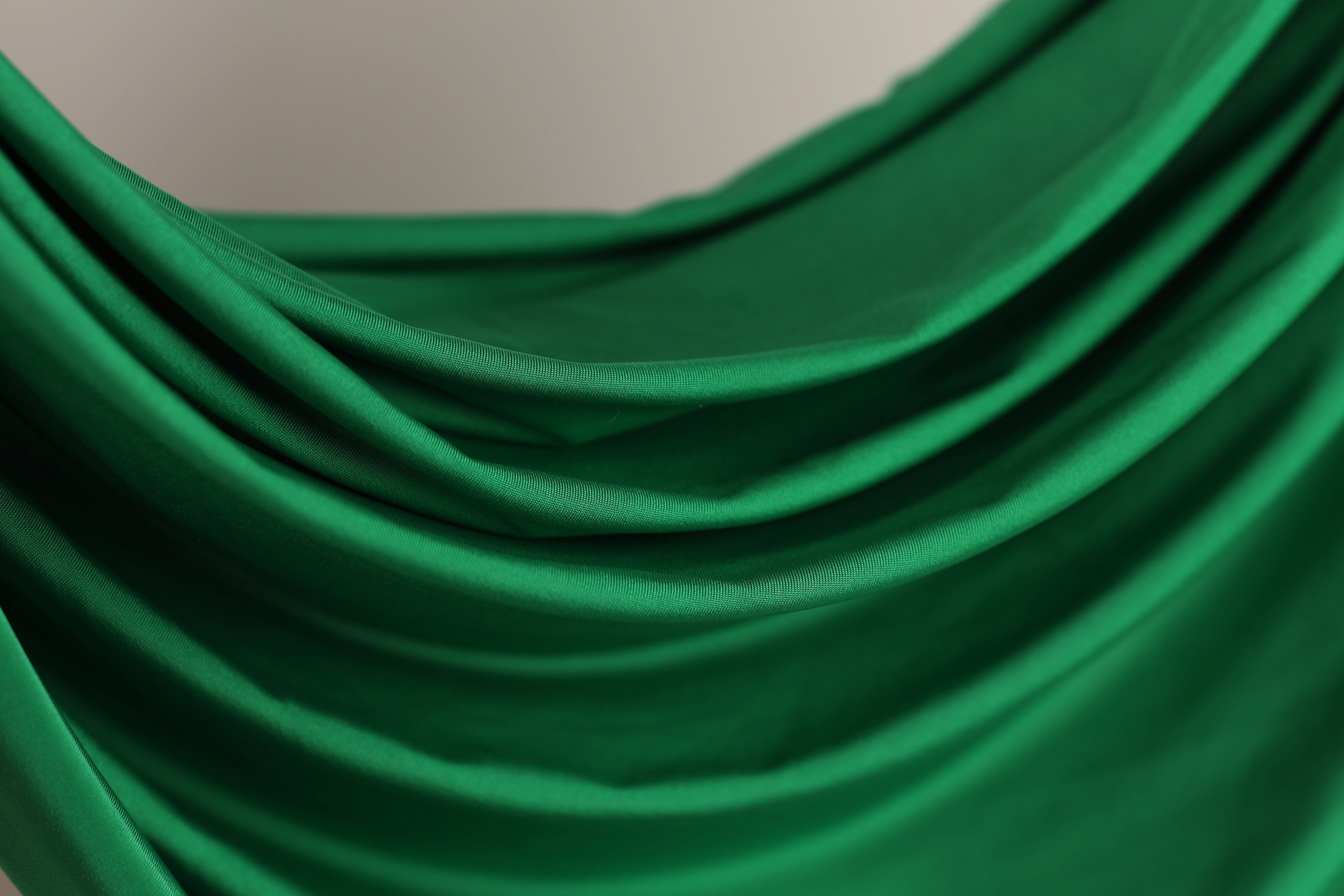 The image is a close-up of a green fabric, possibly silk or chiffon, with a smooth, flowing texture.