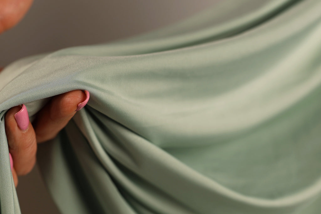 A hand holding a green fabric, with the fingers visible and the thumb curled around the fabric.