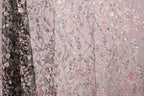 a close-up view of a fabric with a floral pattern, including pink, green, and white flowers and leaves. The fabric appears to be a sheer material, with a dark background that contrasts with the lighter colors of the floral design.