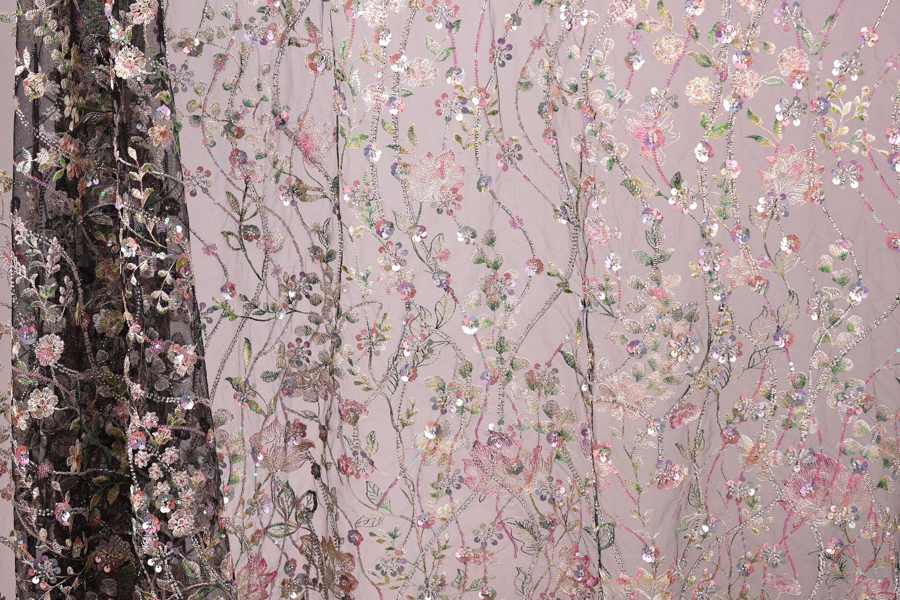 a close-up view of a fabric with a floral pattern, including pink, green, and white flowers and leaves. The fabric appears to be a sheer material, with a dark background that contrasts with the lighter colors of the floral design.