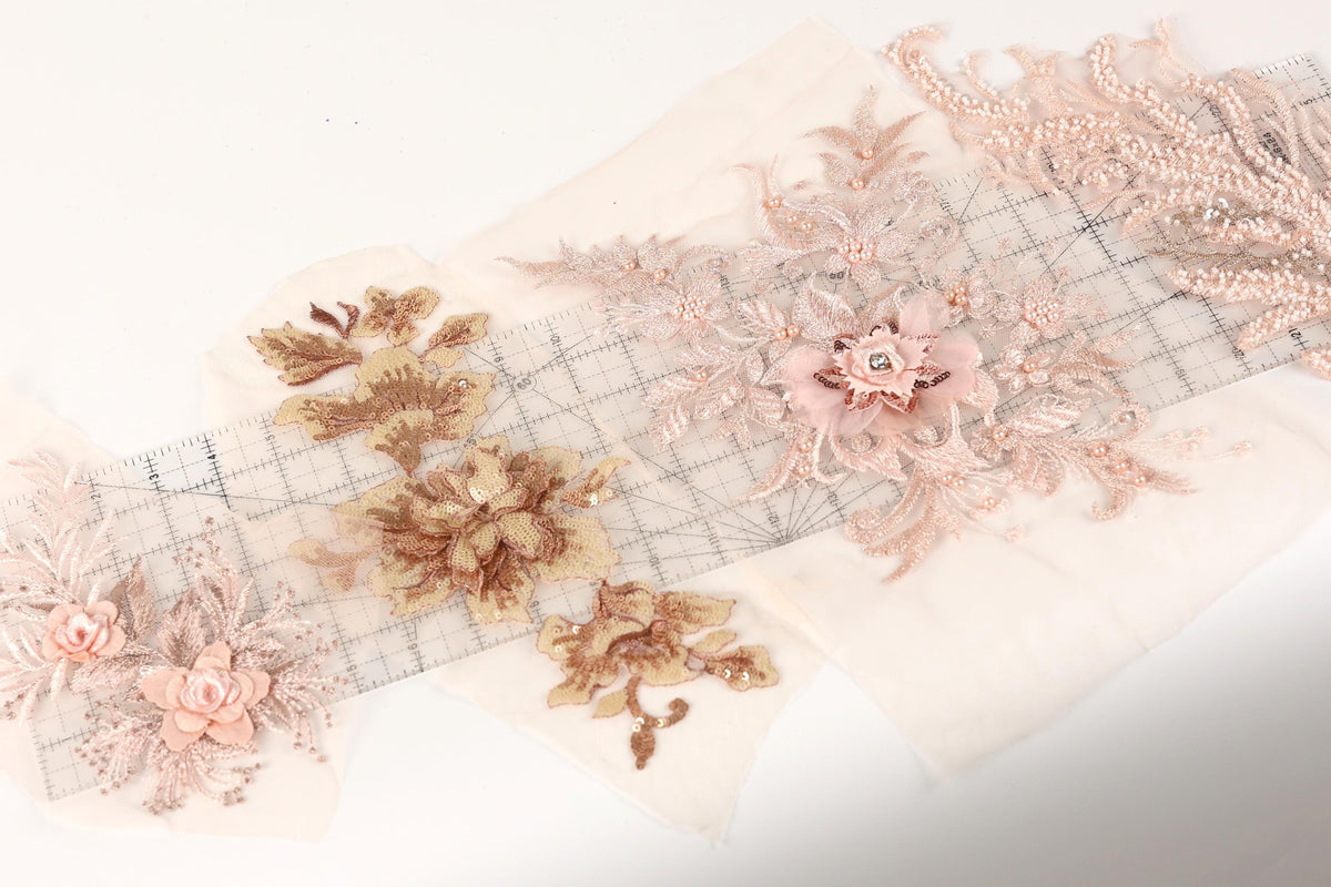 a collection of delicate, intricate floral embroidery pieces, including a large pink flower and smaller pink flowers, arranged on a white background.