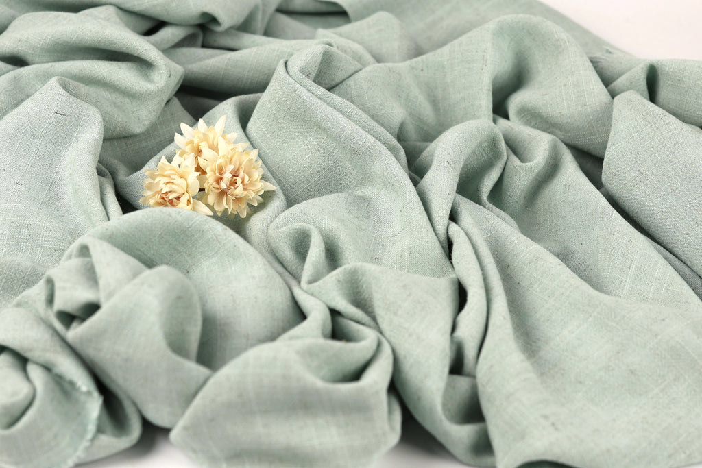 a close-up view of a light green fabric with a small yellow flower resting on it.