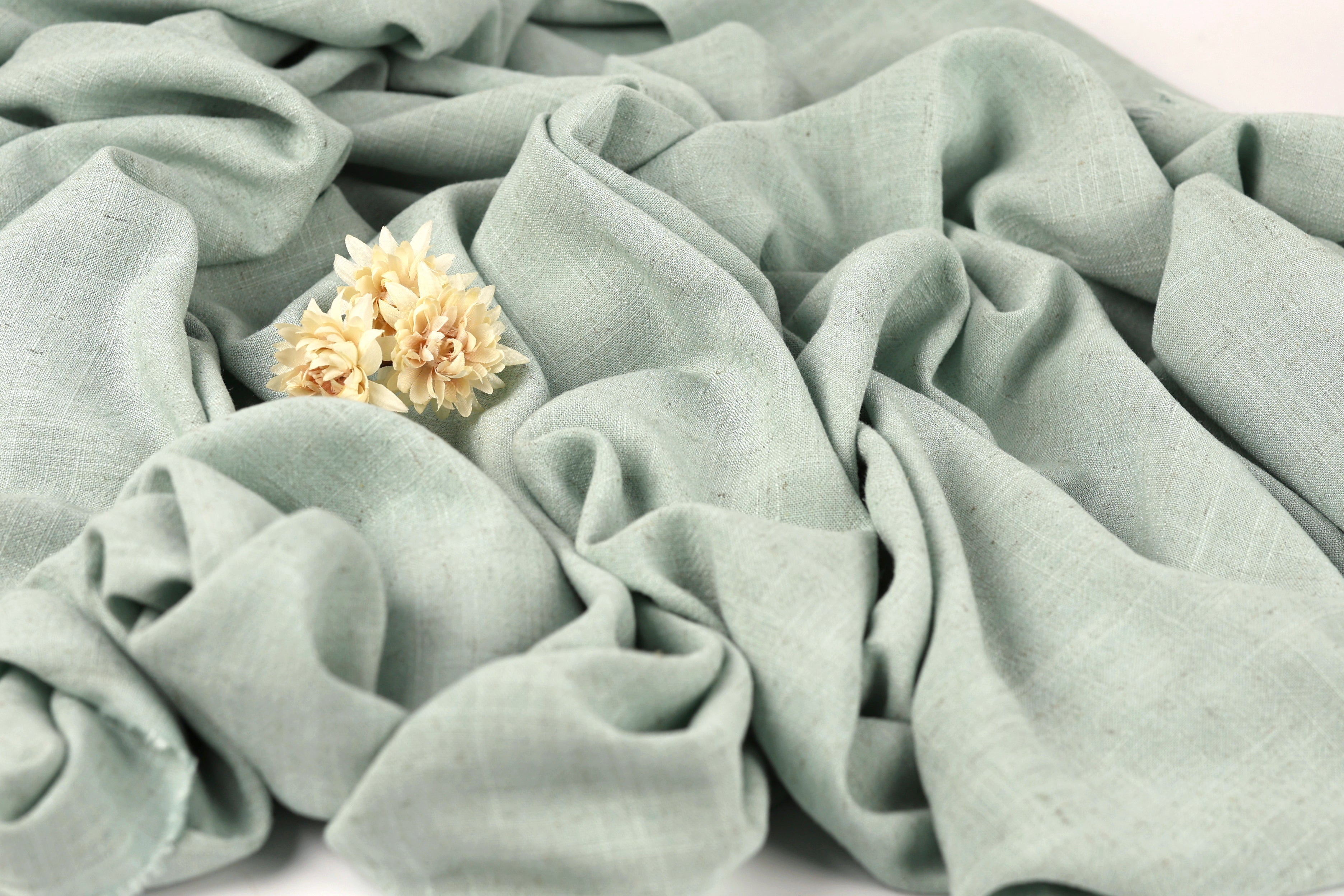 a close-up view of a light green fabric with a small yellow flower resting on it.