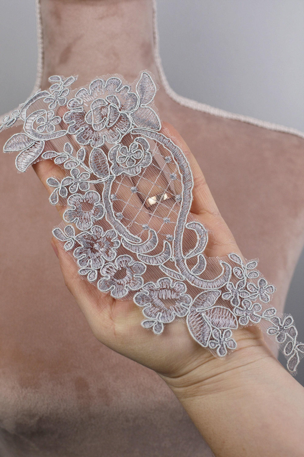 A hand holding a delicate, intricately designed silver lace piece with floral patterns.