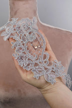 A hand holding a delicate, intricately designed silver lace piece with floral patterns.