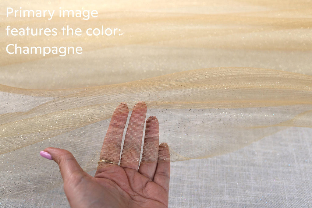A hand is holding up a piece of fabric with a gold glittery texture, and the background is a light beige color.