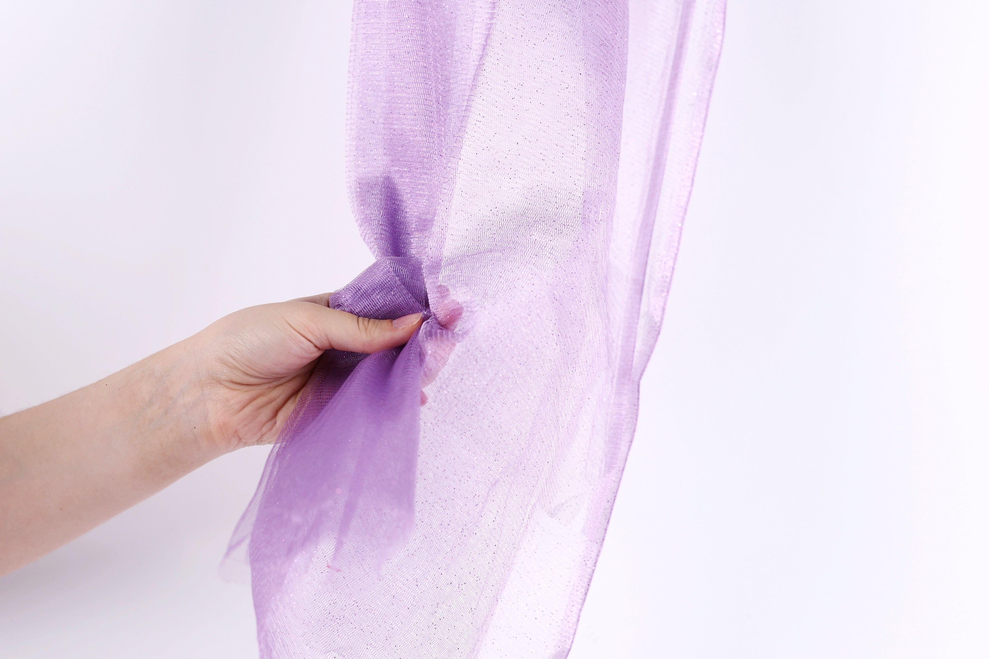 A hand is holding a purple tulle fabric against a white background.