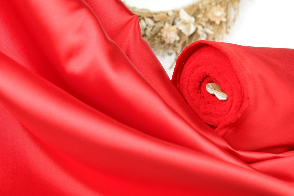 A close-up view of a vibrant red fabric, possibly silk or satin, with a small white object, possibly a button or a decorative element, partially visible in the center.