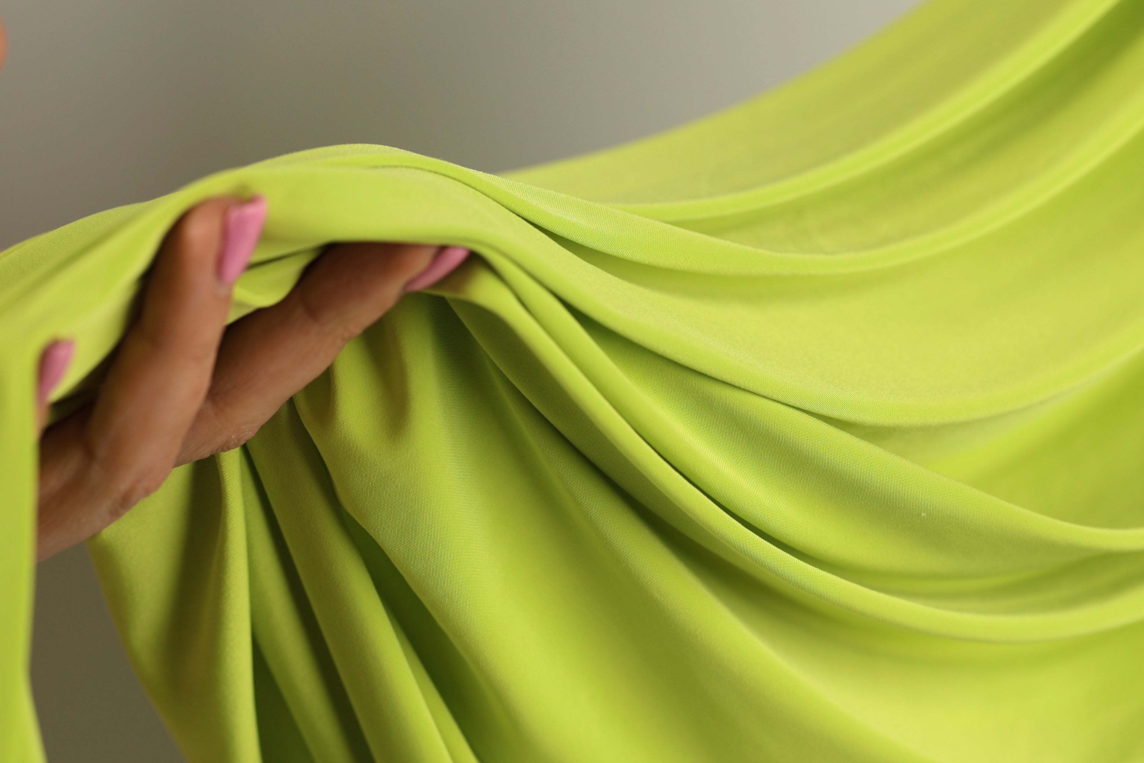 A hand is holding a bright green fabric, which appears to be a soft, flowing material.