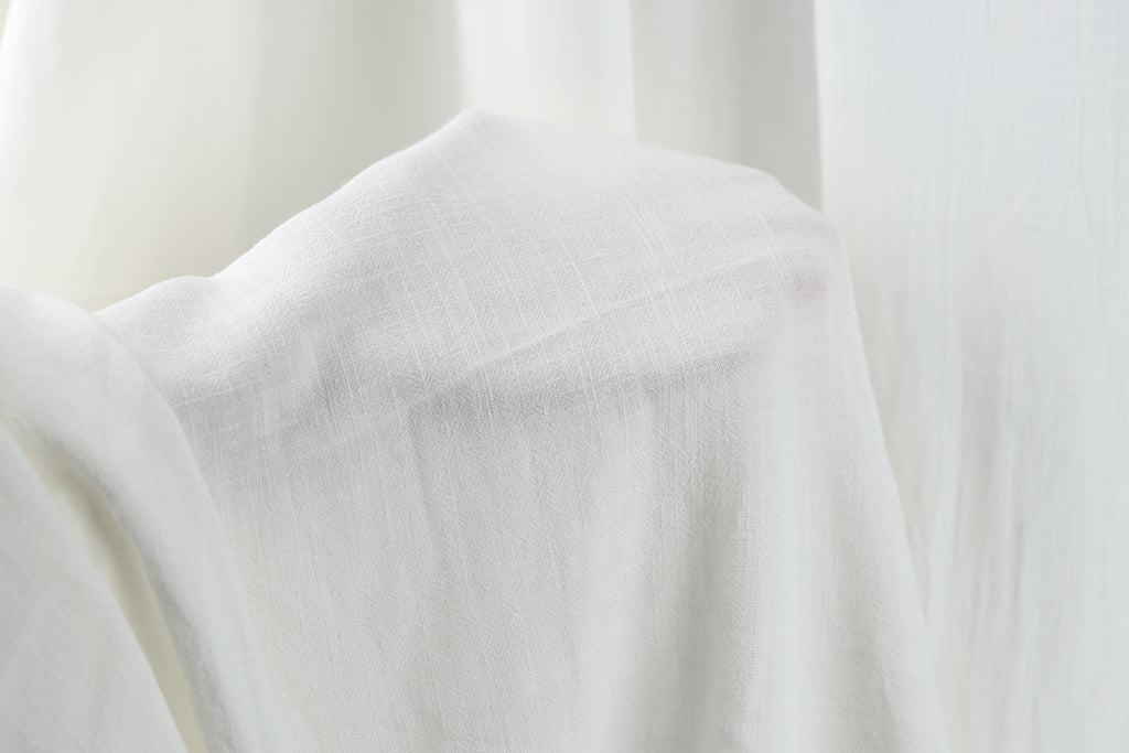 A close-up view of a white fabric, possibly a piece of clothing or a sheer curtain, with a soft, flowing texture.