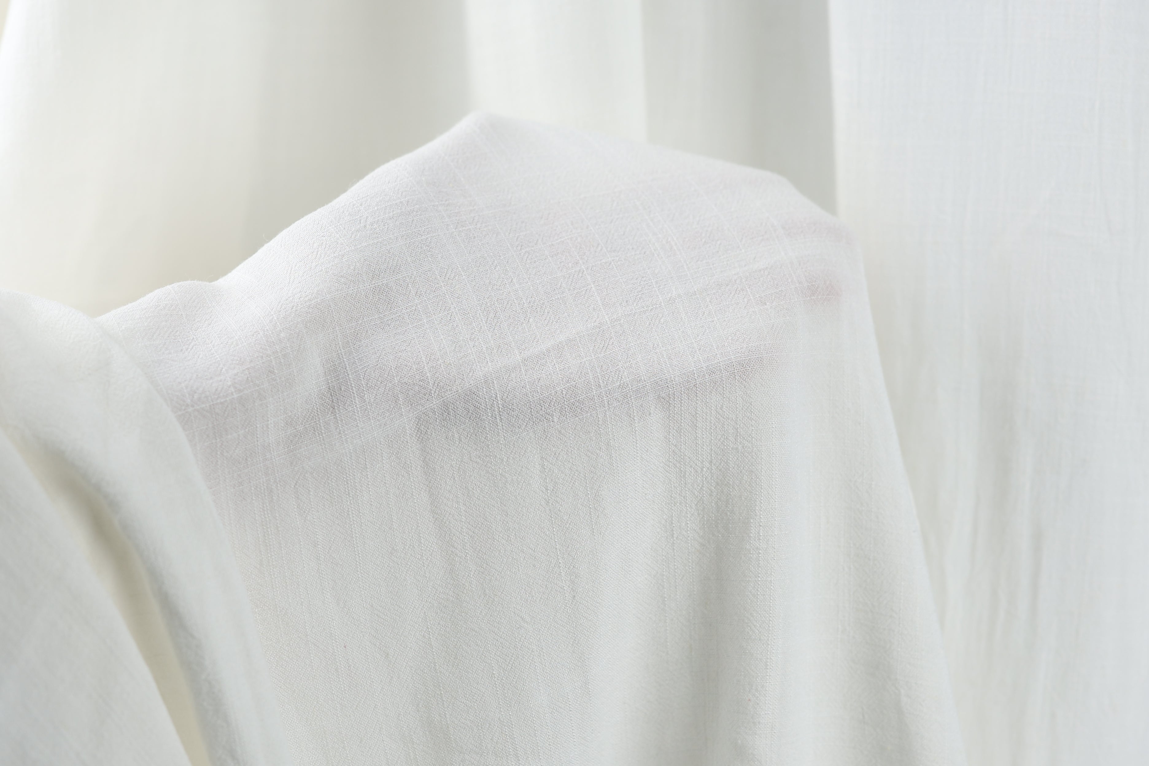 A close-up view of a white fabric, possibly a piece of clothing or a sheer curtain, with a soft, flowing texture.