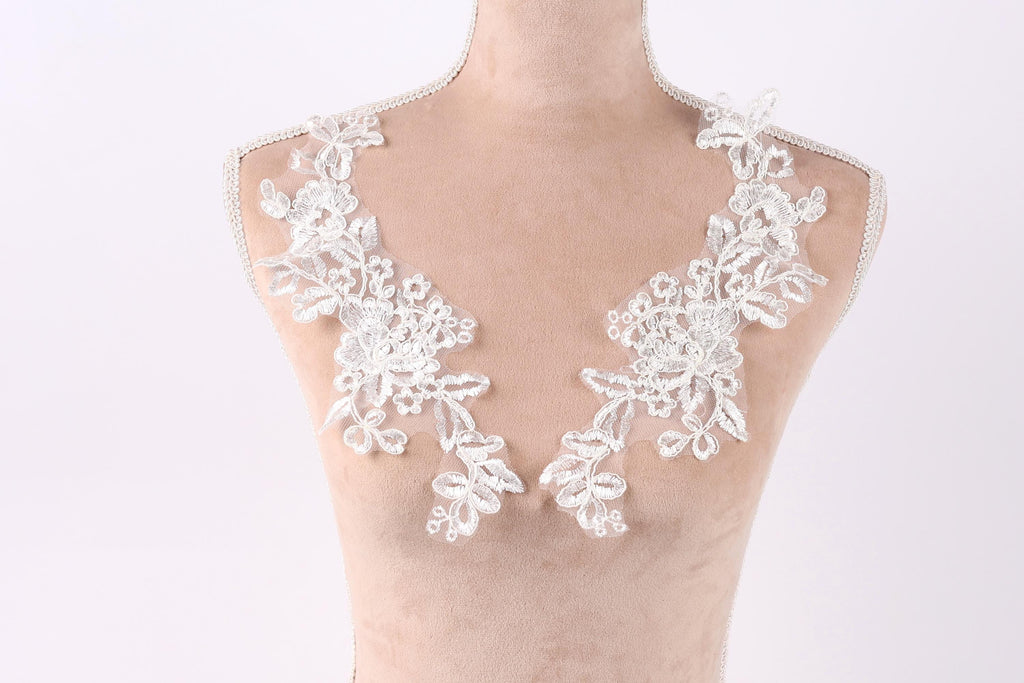 A mannequin wearing a white lace dress with intricate floral embroidery on the shoulders.