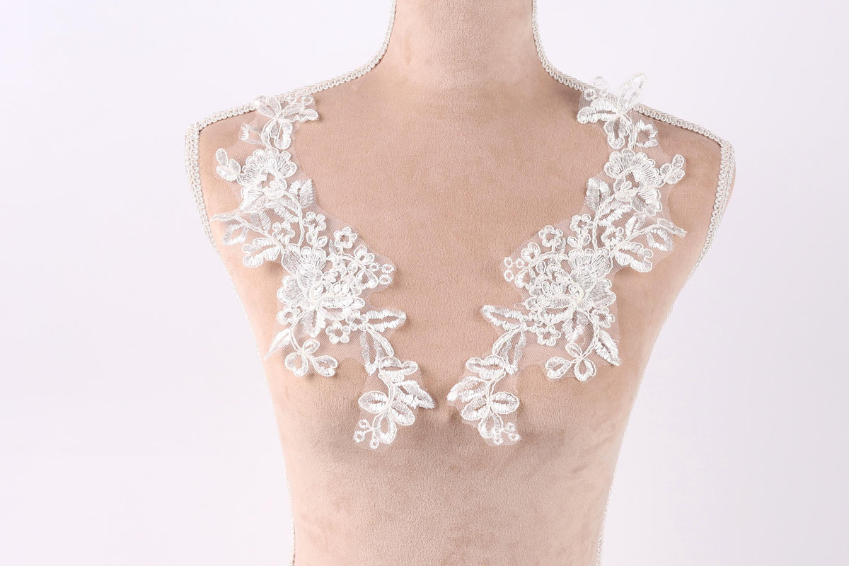 A mannequin wearing a white lace dress with intricate floral embroidery on the shoulders.