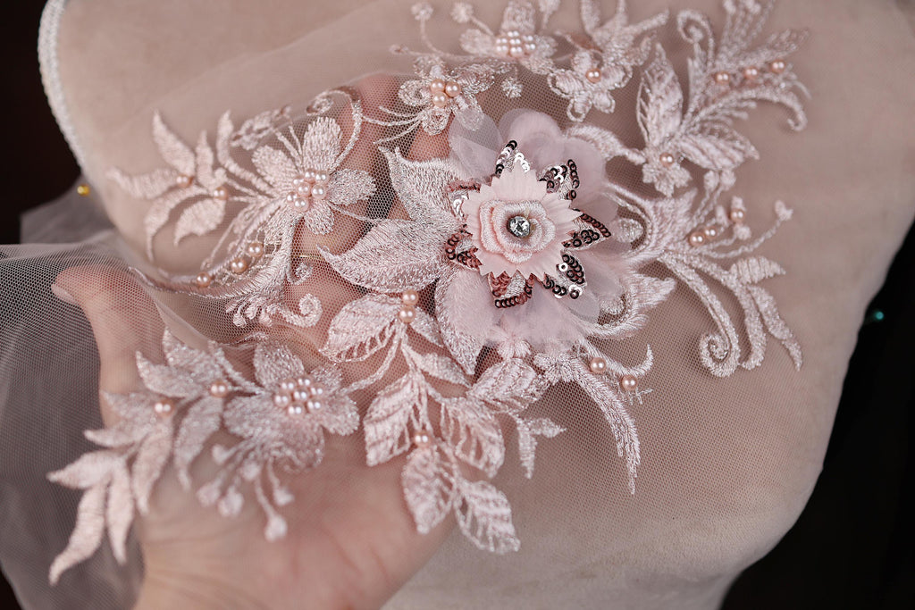 A hand holding a delicate, intricately embroidered piece of lace with a flower design.