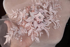 A hand holding a delicate, intricately embroidered piece of lace with a flower design.