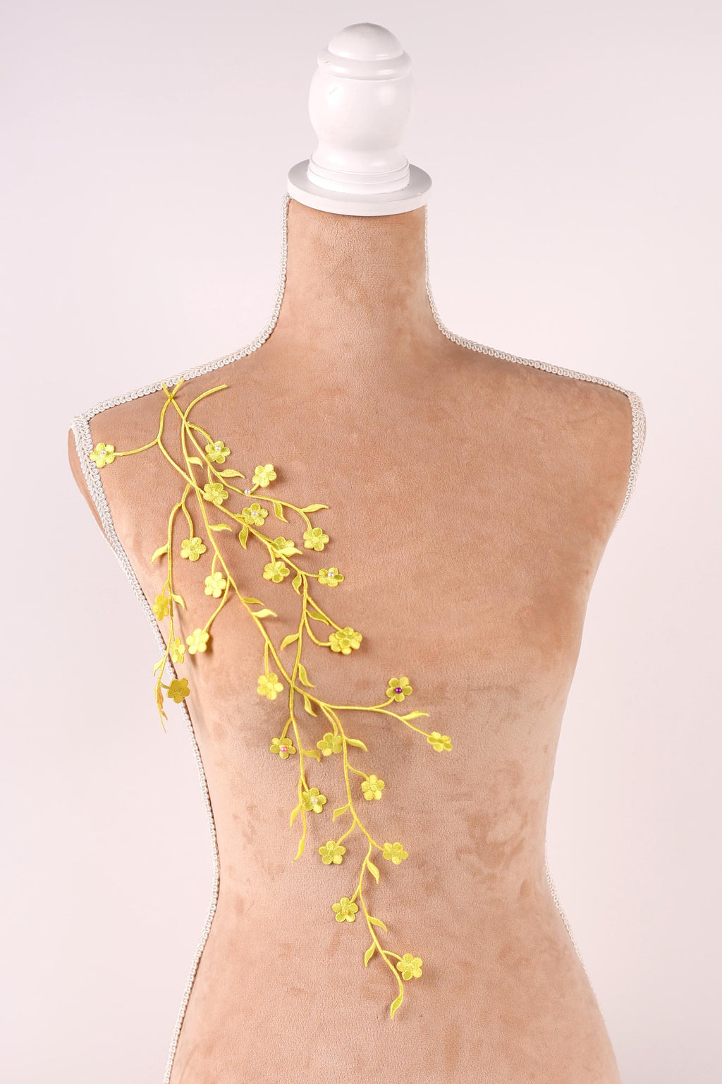 A mannequin with a white head and a beige body, adorned with yellow floral branches hanging from the shoulder.