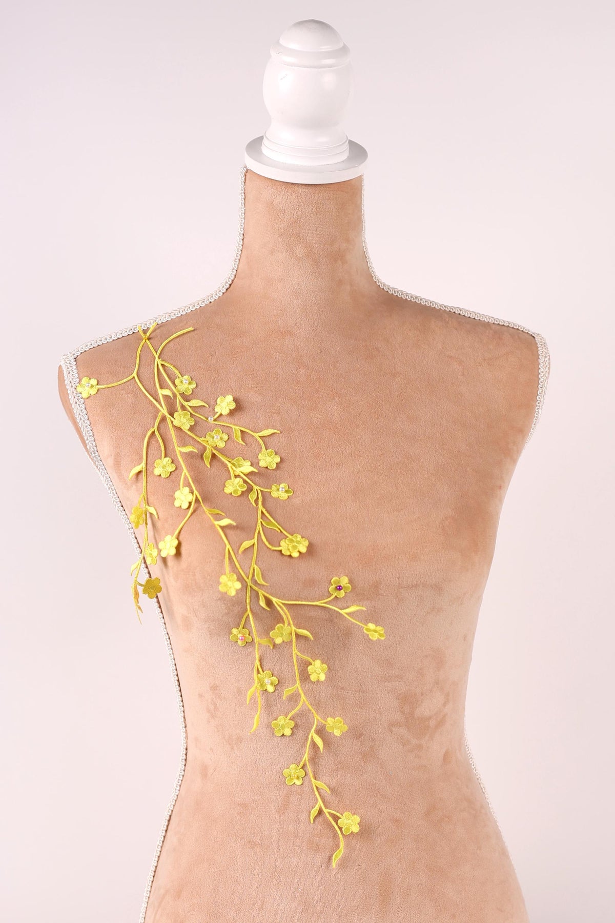 A mannequin with a white head and a beige body, adorned with yellow floral branches hanging from the shoulder.