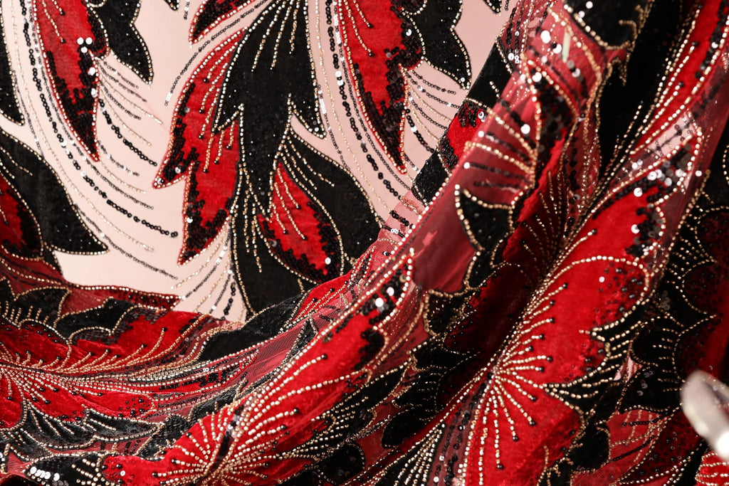 The image is a close-up of a fabric with a red and black floral pattern, featuring sequins and beads. The fabric appears to be a sheer material, with a textured and shiny appearance.