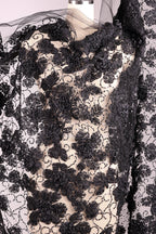 a close-up view of a black and white lace fabric with a floral pattern. The fabric appears to be made of a sheer material, giving it a delicate and elegant appearance.