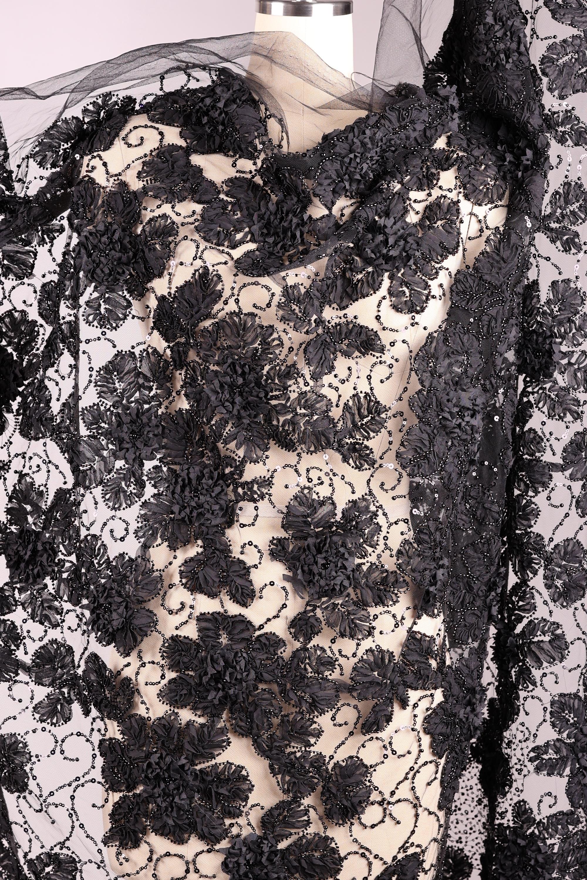 a close-up view of a black and white lace fabric with a floral pattern. The fabric appears to be made of a sheer material, giving it a delicate and elegant appearance.
