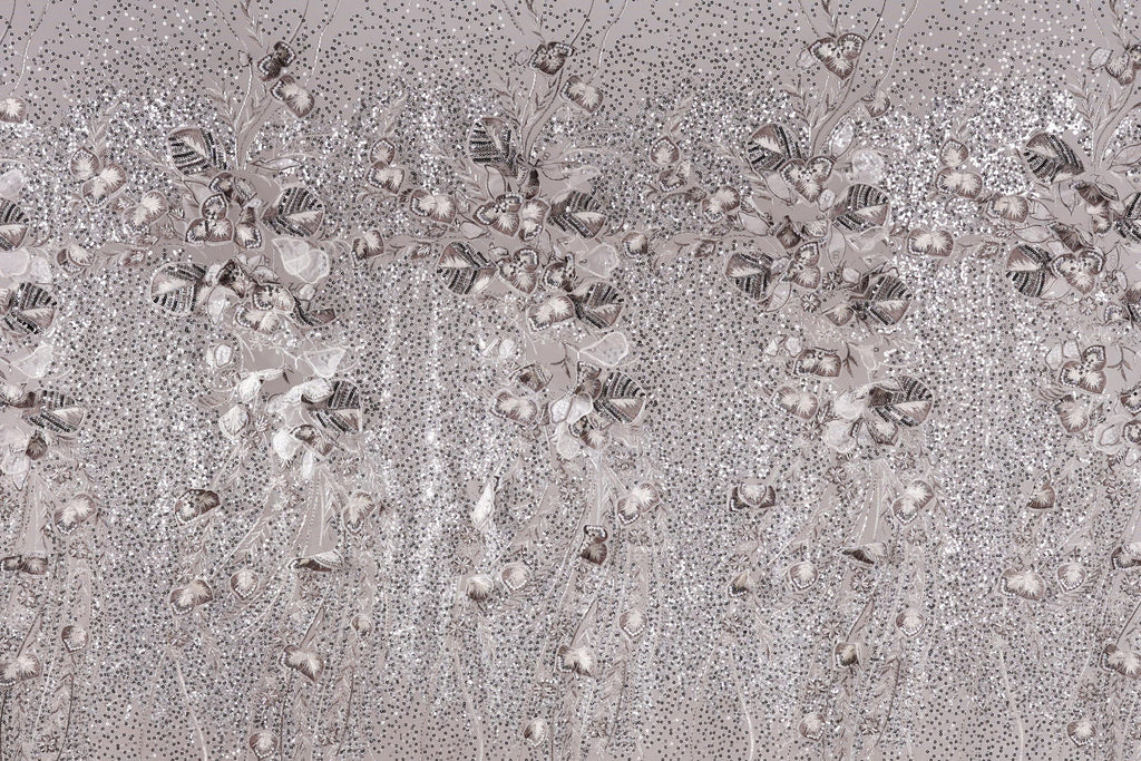 The image is a close-up of a fabric with a repeating pattern of small white and gray flowers or leaves, creating a textured and visually interesting surface.