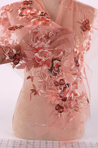 a mannequin wearing a pink dress with intricate floral embroidery. The dress has a sheer, flowy design with a pink and red floral pattern that covers the entire dress. The mannequin is positioned in a way that showcases the dress's design and details.