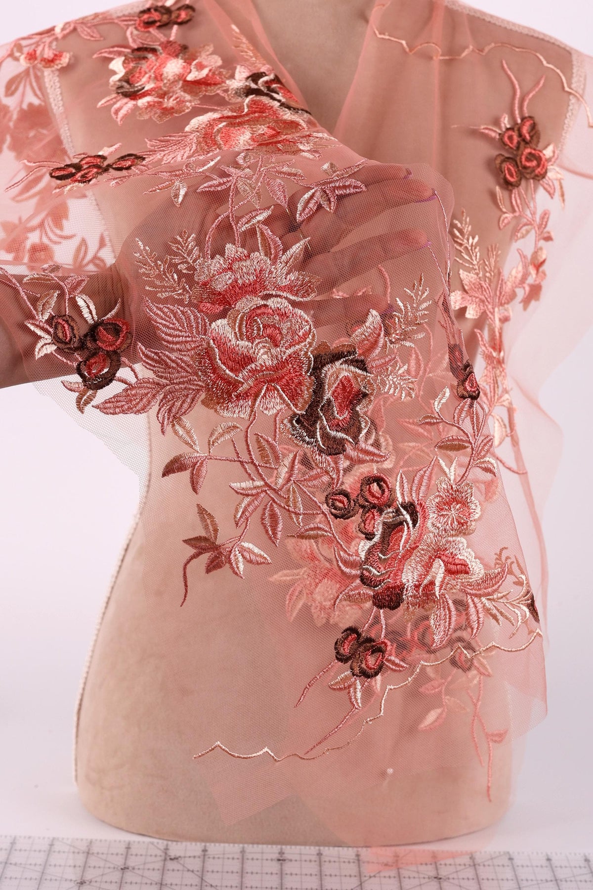 a mannequin wearing a pink dress with intricate floral embroidery. The dress has a sheer, flowy design with a pink and red floral pattern that covers the entire dress. The mannequin is positioned in a way that showcases the dress's design and details.