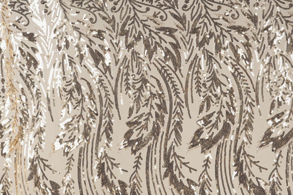 a close-up view of a fabric with a repeating pattern of brown and white sequin designs. The pattern appears to be a floral or leaf-like design, with the sequins arranged in a way that creates a sense of movement and texture. The fabric has a beige background, which contrasts with the dark brown and white colors of the sequins. The image does not contain any text or other discernible objects, and the positioning of the sequins suggests a random or organic arrangement.
