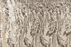 a close-up view of a fabric with a repeating pattern of brown and white sequin designs. The pattern appears to be a floral or leaf-like design, with the sequins arranged in a way that creates a sense of movement and texture. The fabric has a beige background, which contrasts with the dark brown and white colors of the sequins. The image does not contain any text or other discernible objects, and the positioning of the sequins suggests a random or organic arrangement.