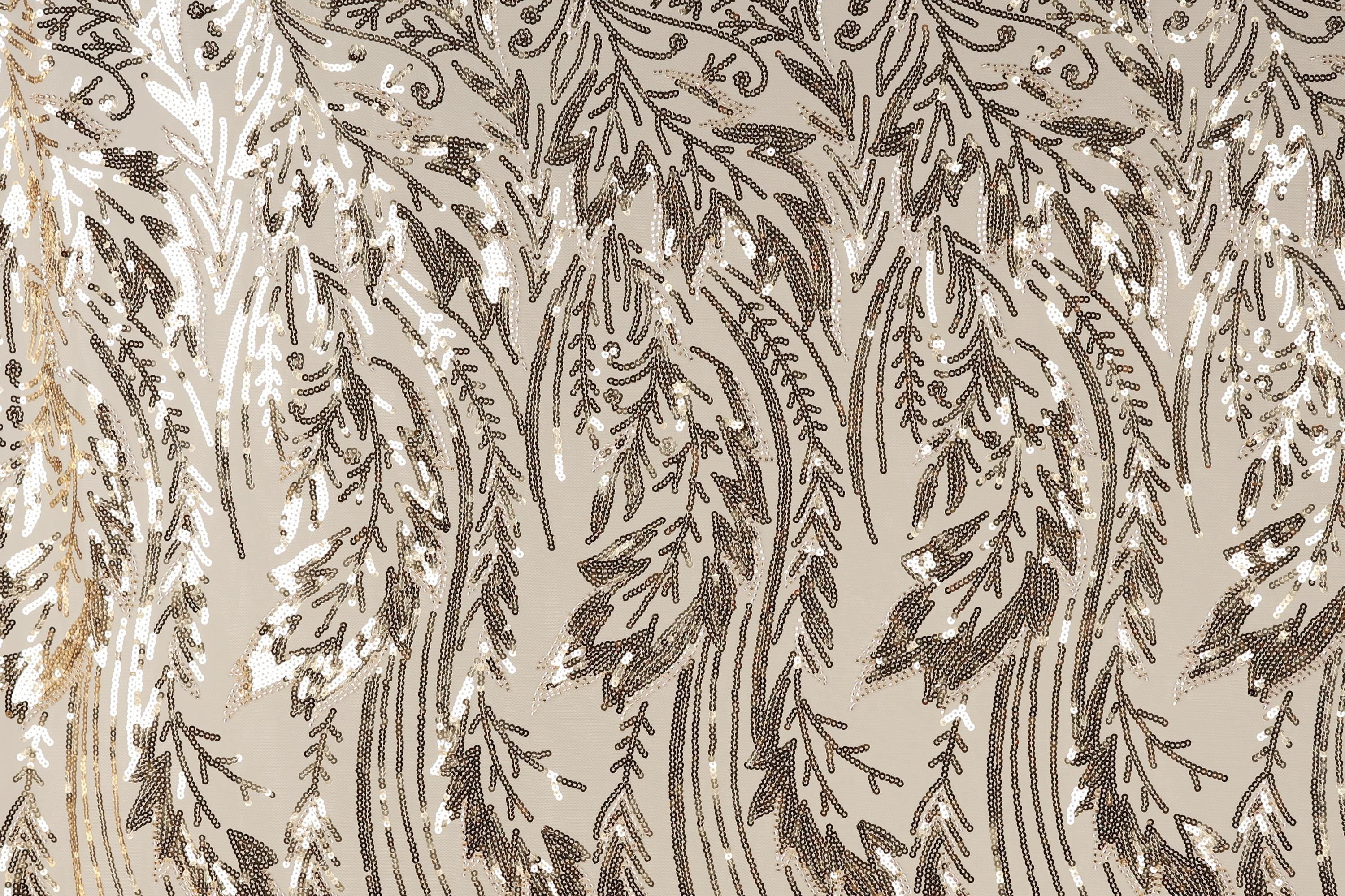 a close-up view of a fabric with a repeating pattern of brown and white sequin designs. The pattern appears to be a floral or leaf-like design, with the sequins arranged in a way that creates a sense of movement and texture. The fabric has a beige background, which contrasts with the dark brown and white colors of the sequins. The image does not contain any text or other discernible objects, and the positioning of the sequins suggests a random or organic arrangement.