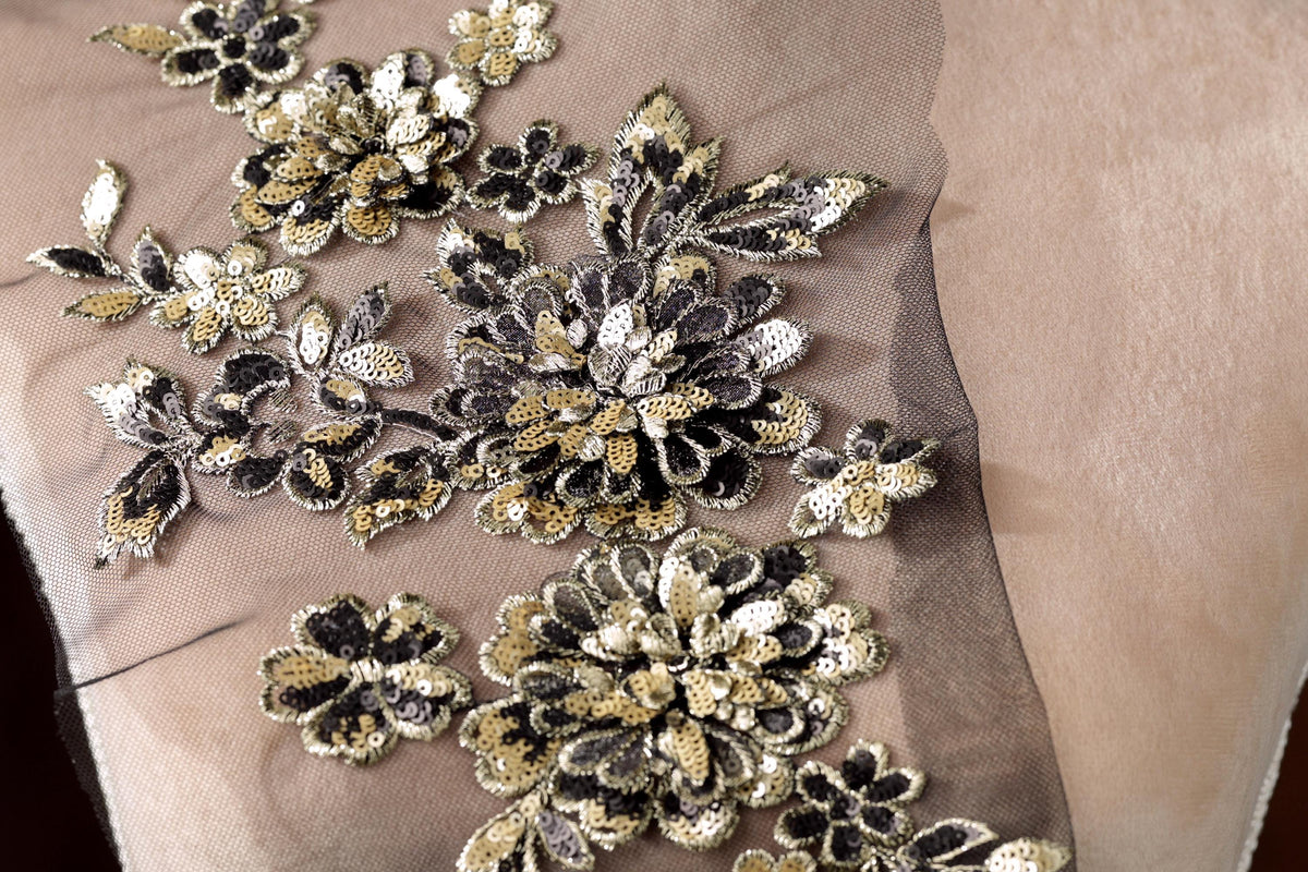 a close-up view of a delicate, intricate floral embroidery on a fabric surface. The embroidery is composed of numerous small, black and gold flowers arranged in a visually appealing pattern. The flowers are intricately detailed, showcasing the skill and craftsmanship of the embroiderer. The fabric appears to be a light-colored material, possibly a sheer or sheer-like fabric, which complements the delicate appearance of the flowers.