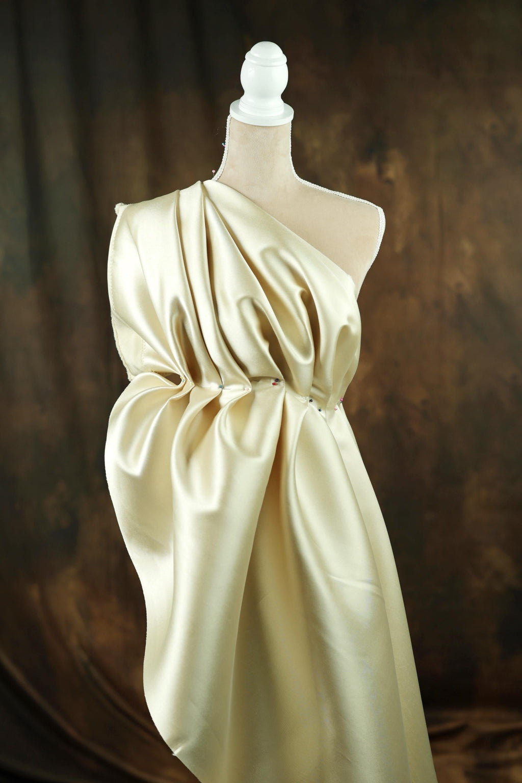 A mannequin wearing a gold satin dress with a draped, flowing design.