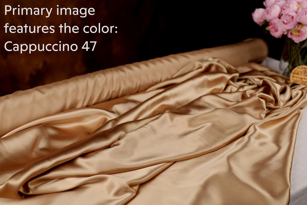 a roll of golden satin fabric with a floral arrangement of pink flowers in the background.