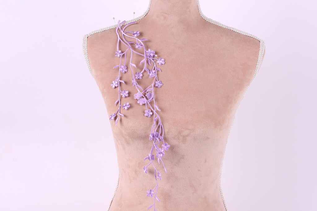 A mannequin with a delicate floral decoration on its back, featuring a long, trailing purple branch with small purple flowers.