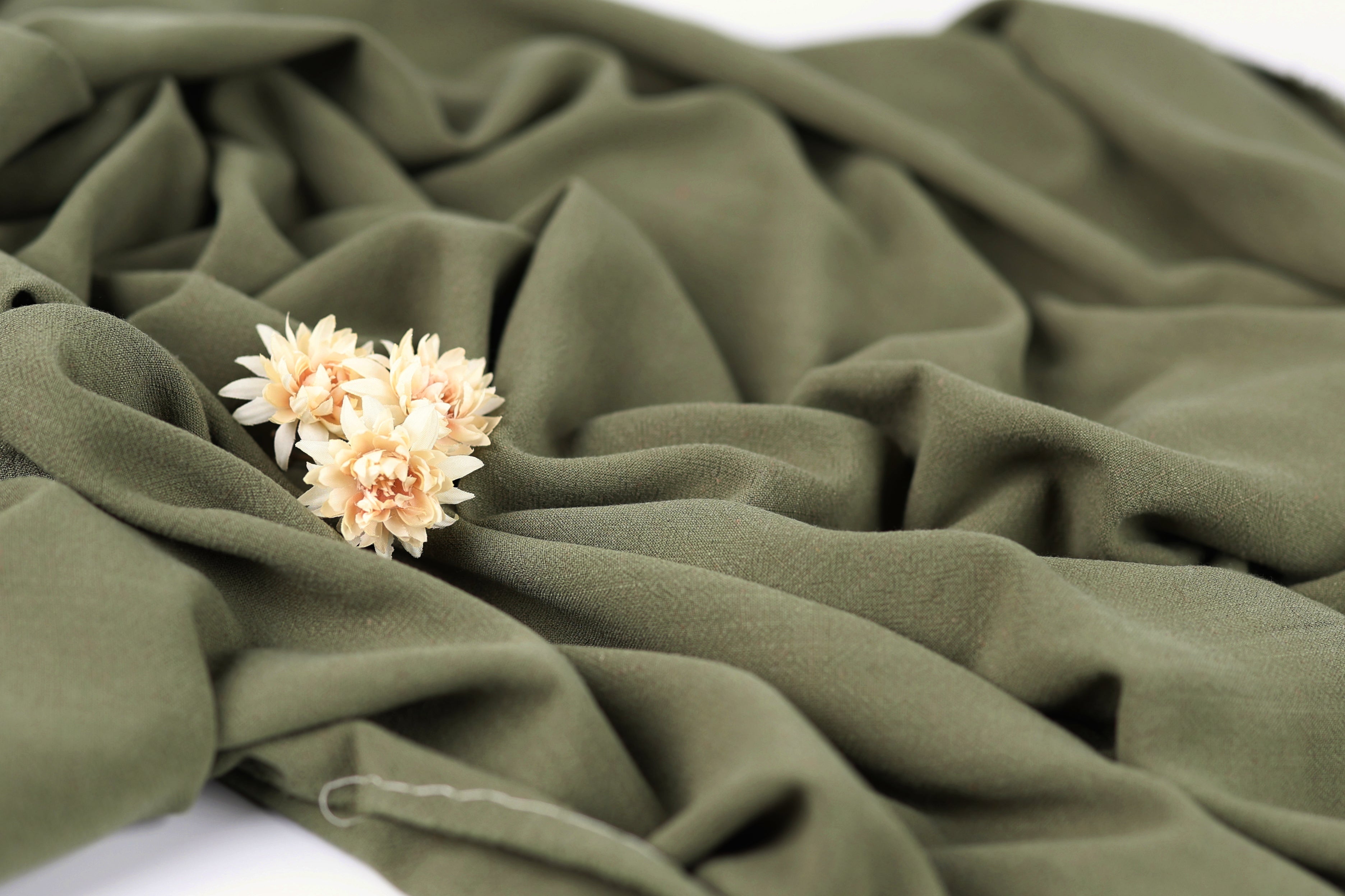 A close-up view of a green fabric with a delicate flower resting on it.