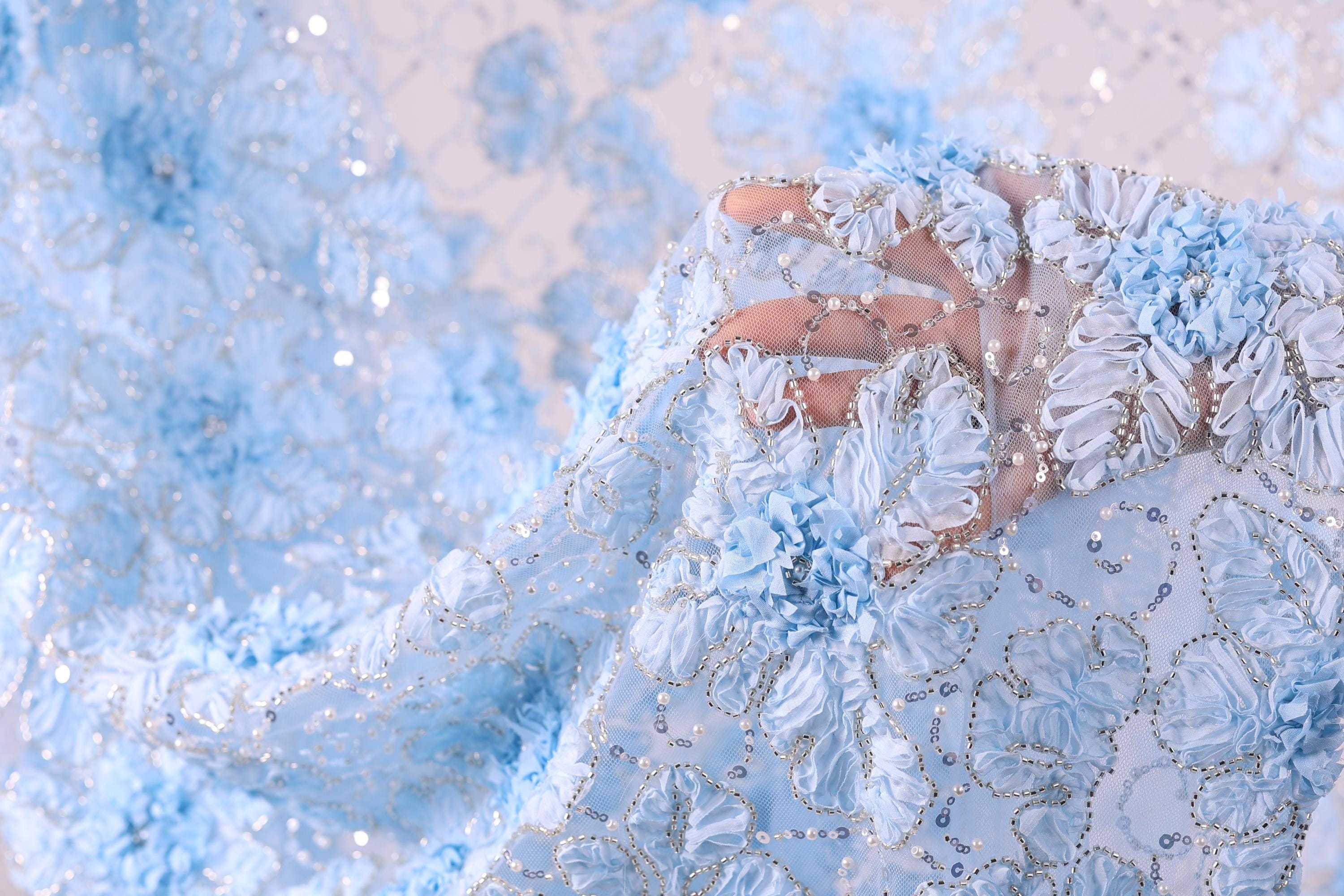 A close-up view of a delicate, intricately embroidered fabric with a floral pattern in shades of blue and white.