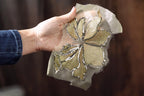 A hand holding a piece of fabric with a gold and beige floral design.