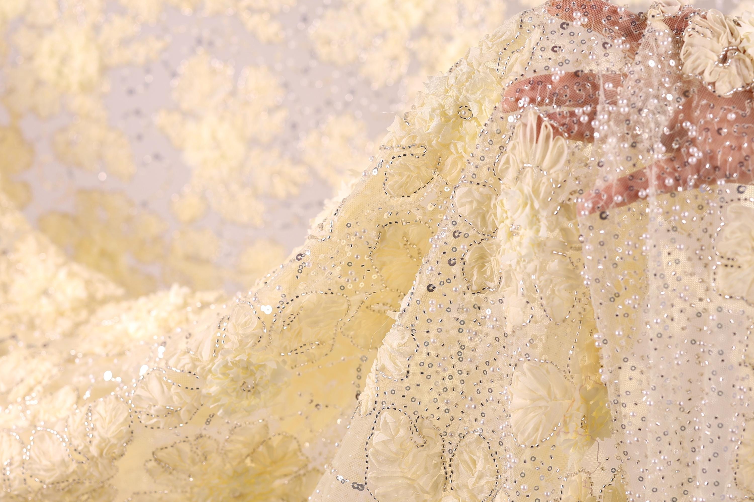 A close-up view of a hand holding a piece of fabric with a delicate, intricate floral pattern.