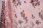 a close-up view of a fabric with a pink and black floral pattern. The fabric appears to be made of sequin material, with a mix of pink and black sequins visible throughout the design. The pattern is intricate and detailed, showcasing the craftsmanship of the fabric.