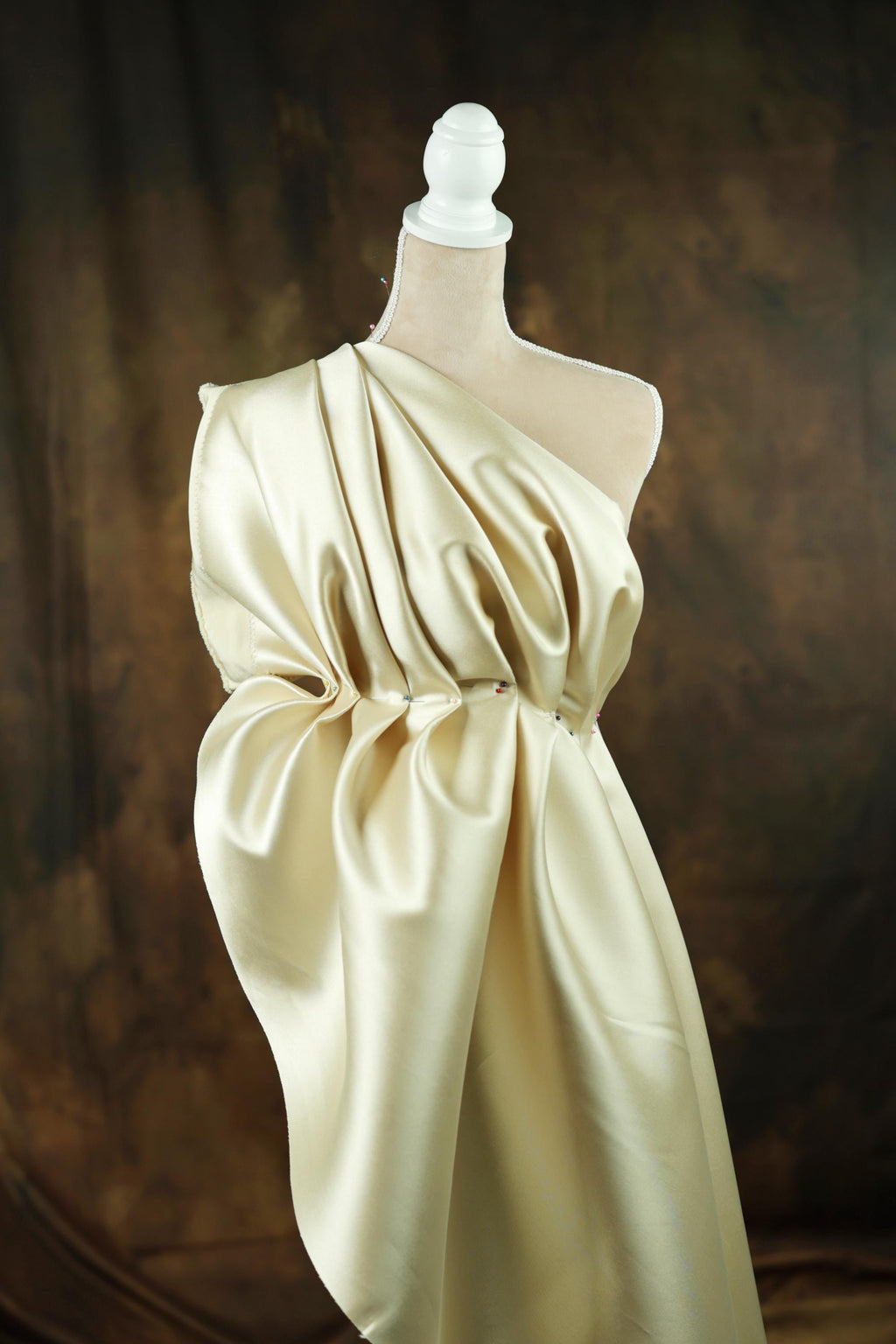 A mannequin wearing a one-shoulder dress made of a shiny, draped fabric.