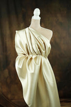 A mannequin wearing a one-shoulder dress made of a shiny, draped fabric.